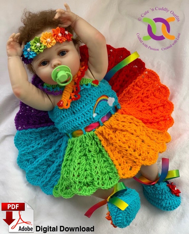 Puede incluir: Un vestido de crochet arco&iacute;ris y zapatos a juego para una mu&ntilde;eca beb&eacute;. El vestido tiene un dise&ntilde;o de arco&iacute;ris con una flor blanca de crochet en la parte delantera. Los zapatos tambi&eacute;n son de crochet y tienen una cinta de arco&iacute;ris.