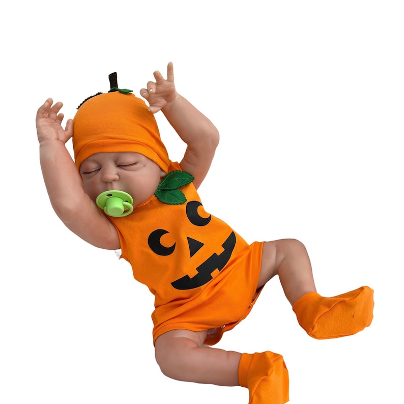 May include: A baby wearing an orange pumpkin costume with a black jack-o'-lantern face. The costume includes a hat, a sleeveless onesie, and booties. The baby is wearing a green pacifier.