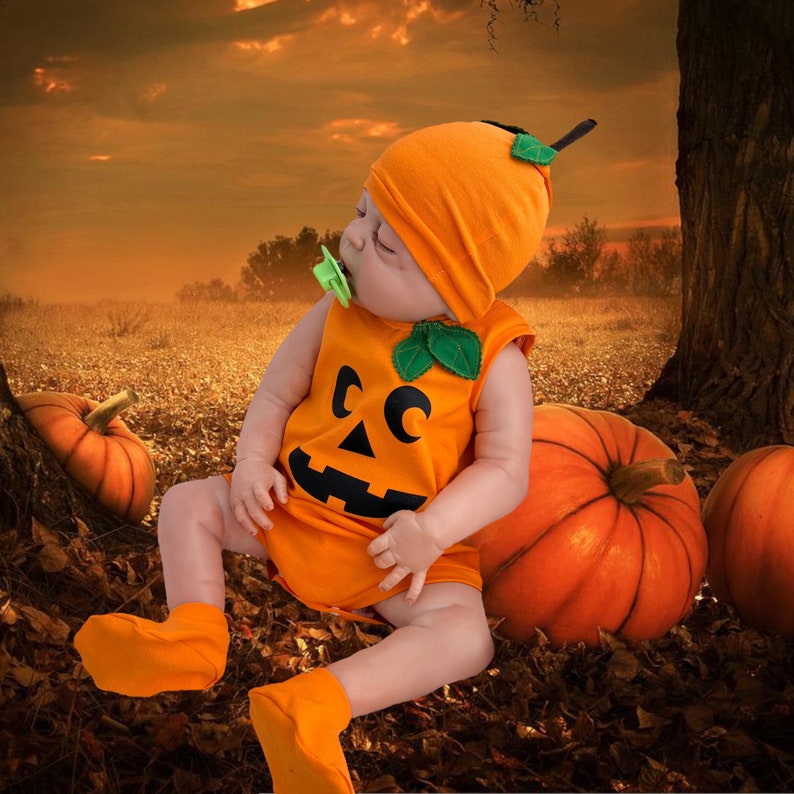 May include: A baby wearing an orange pumpkin costume with a green leaf and a black jack-o'-lantern face. The baby is sitting on a bed of fall leaves with two pumpkins beside them.