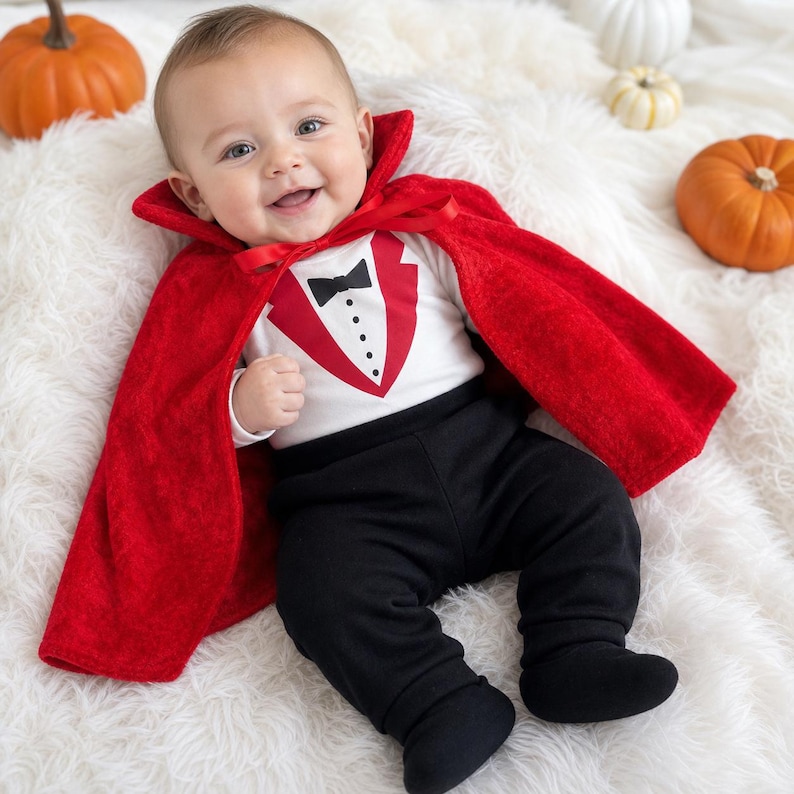 May include: A baby outfit consisting of a white long-sleeve shirt with a printed red tuxedo vest, black bowtie, and buttons, paired with solid black footed pants and a bright red velvet cape that features a high collar and a red ribbon tie.
