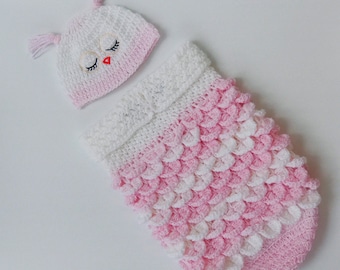 May include: A pink and white crocheted baby outfit with an owl-shaped hat. The hat has embroidered eyes and a beak.