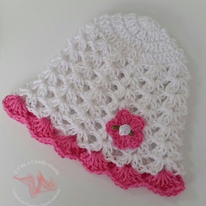 May include: White crochet sun hat with a pink crocheted flower and a pink crocheted trim. The hat is made with a delicate, open stitch pattern.