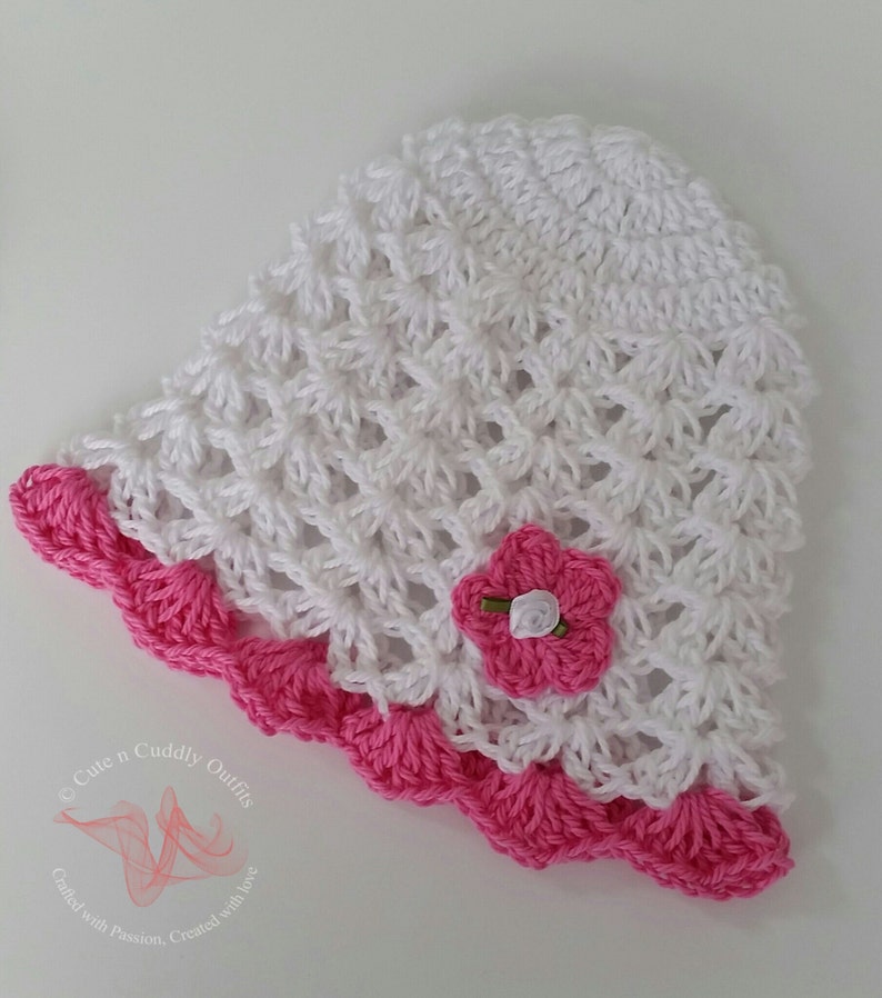 May include: White crochet sun hat with a pink crocheted flower and a pink crocheted trim. The hat is made with a delicate, open stitch pattern.
