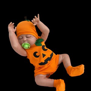 May include: A baby doll wearing an orange pumpkin costume with a green leaf and black facial features. The doll is wearing a pacifier.