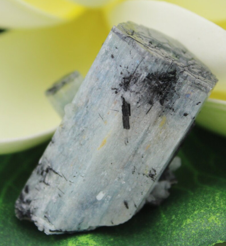 Puede incluir: Un cristal de aguamarina azul claro con inclusiones negras. El cristal es &aacute;spero y tiene un aspecto natural sin pulir.