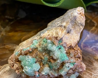 May include: A rough, gray rock with a cluster of green and white crystals. The crystals are clustered together in a dense formation.