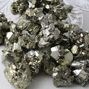 May include: A pile of raw, unpolished pyrite crystals. The crystals are a metallic gold color and have a rough, textured surface.
