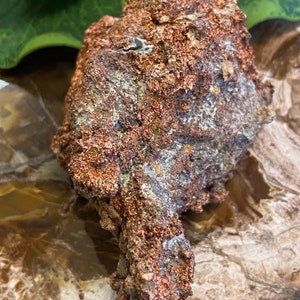 Puede incluir: Una roca grande, rugosa, de color cobre con un brillo met&aacute;lico. La roca tiene una forma &uacute;nica, irregular y una superficie texturizada.