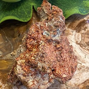 Puede incluir: Una pepita de cobre rugosa, de color marr&oacute;n rojizo, con una forma natural irregular. El cobre tiene un brillo met&aacute;lico y est&aacute; cubierto de peque&ntilde;as formaciones cristalinas.