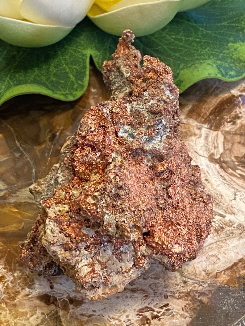 Puede incluir: Una pepita de cobre rugosa, de color marr&oacute;n rojizo, con una forma natural irregular. El cobre tiene un brillo met&aacute;lico y est&aacute; cubierto de peque&ntilde;as formaciones cristalinas.