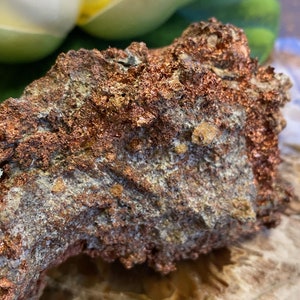Puede incluir: Primer plano de una roca rugosa de color cobre con una superficie texturizada. La roca tiene un brillo met&aacute;lico y parece ser un mineral natural.