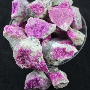 May include: A collection of pink and gray rough crystals in a glass bowl. The crystals have a sparkly, iridescent finish.