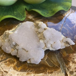 May include: A cluster of white and light purple crystals on a rough, brown rock. The crystals have a sparkly, frosted appearance.