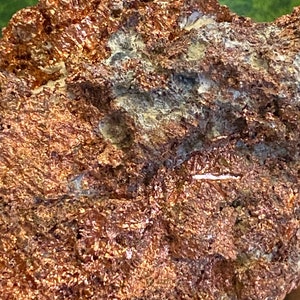 Puede incluir: Primer plano de una roca rugosa de color cobre con una textura cristalina blanca. La roca tiene un aspecto natural y terroso.