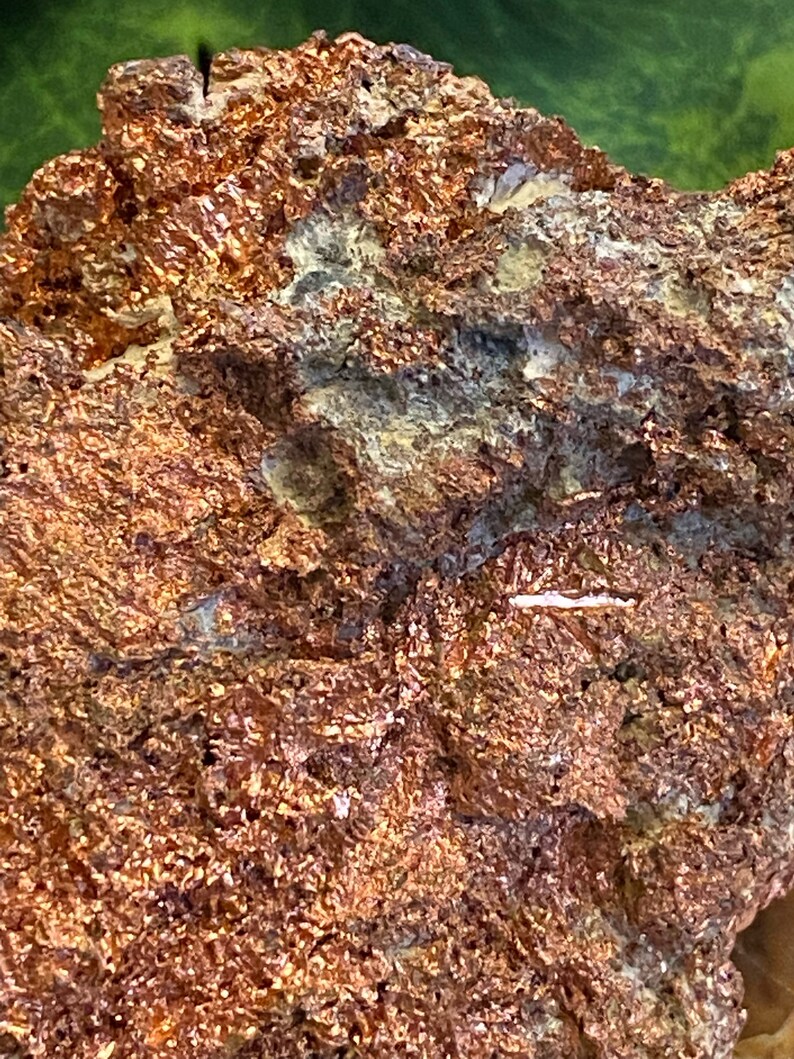 Puede incluir: Primer plano de una roca rugosa de color cobre con una textura cristalina blanca. La roca tiene un aspecto natural y terroso.