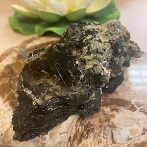 May include: A large, dark brown and green crystal with a rough, textured surface. The crystal has a layered appearance and is partially covered in smaller, green crystals.