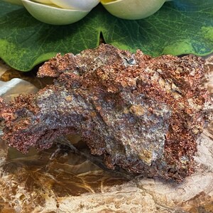 Puede incluir: Una roca grande, rugosa, de color cobre con un brillo met&aacute;lico. La roca tiene una variedad de texturas y formas, con algunas &aacute;reas que parecen m&aacute;s lisas y otras m&aacute;s irregulares. La roca est&aacute; descansando sobre una superficie marr&oacute;n y texturizada.