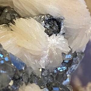 May include: Close-up of a cluster of white barite crystals with a small cluster of black and silver galena crystals in the center.