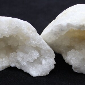 May include: Two halves of a white geode with a crystal-lined interior. The geode is a natural rock formation with a hollow cavity lined with crystals.