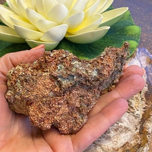 Puede incluir: Una roca grande, rugosa, de color cobre con un brillo met&aacute;lico. La roca tiene una forma irregular y dentada y est&aacute; cubierta de peque&ntilde;as formaciones cristalinas.