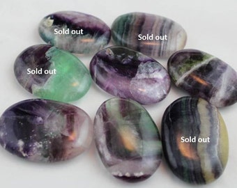 Puede incluir: Siete piedras de fluorita pulidas en varios tonos de verde, morado y blanco. Algunas piedras tienen el texto "Sold out" escrito en ellas.