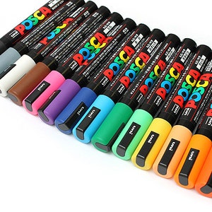 Peut inclure: Un ensemble de 17 marqueurs de peinture Posca de diff&eacute;rentes couleurs, notamment noir, gris, blanc, marron, rose, violet, bleu, turquoise, vert, vert clair, jaune, orange et rouge. Les marqueurs sont dispos&eacute;s en rang&eacute;e de gauche &agrave; droite, le marqueur noir &agrave; gauche et le marqueur rouge &agrave; droite.