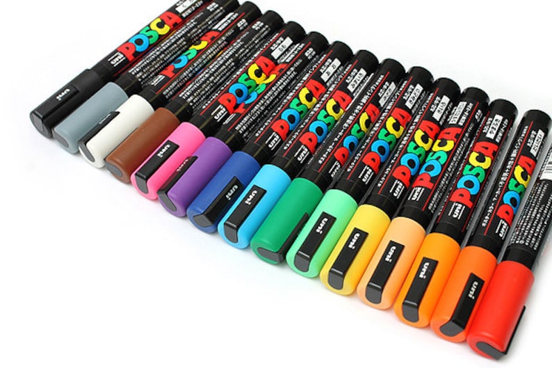 Peut inclure: Un ensemble de 17 marqueurs de peinture Posca de diff&eacute;rentes couleurs, notamment noir, gris, blanc, marron, rose, violet, bleu, turquoise, vert, vert clair, jaune, orange et rouge. Les marqueurs sont dispos&eacute;s en rang&eacute;e de gauche &agrave; droite, le marqueur noir &agrave; gauche et le marqueur rouge &agrave; droite.