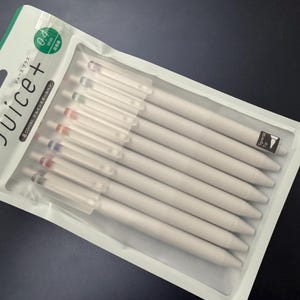 May include: A set of eight Pilot Juice+ gel ink pens in a clear plastic retail package. Each pen has a matte white barrel and a clear cap with a colored clip. The packaging features the text Juice+ and 0.4 mm, indicating the tip size.