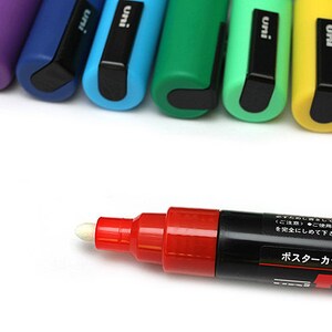 Peut inclure: Gros plan sur un marqueur rouge pour poster avec une pointe blanche. Le marqueur est &eacute;tiquet&eacute; "Poster Color Marker" en japonais. Le marqueur est entour&eacute; d'une rang&eacute;e de marqueurs color&eacute;s avec des bouchons noirs.