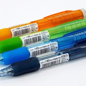 May include: Four mechanical pencils in orange, green, blue, and black with clear barrels. The pencils are labeled "Side FX 0.5mm P025S-CA" and "シャープ 0.5mm P025S-CA".