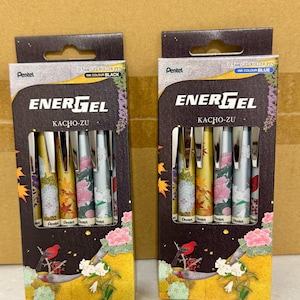 May include: Two Pentel EnerGel Kacho-Zu gel roller pen sets in rectangular boxes. Each box contains five 0.5mm pens with floral and bird patterns. One box features black ink, and the other features blue ink. The packaging displays the brand name EnerGel, the series name Kacho-Zu, and detailed botanical illustrations with small red birds.