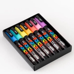 Puede incluir: Un conjunto de ocho marcadores de pintura POSCA de color pastel en una caja negra. Los marcadores est&aacute;n dispuestos en un orden de arco&iacute;ris de azul a morado. La caja tiene el logotipo de POSCA y texto japon&eacute;s.
