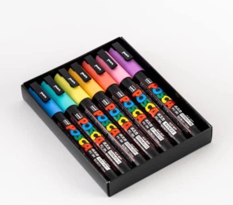 Puede incluir: Un conjunto de ocho marcadores de pintura POSCA de color pastel en una caja negra. Los marcadores est&aacute;n dispuestos en un orden de arco&iacute;ris de azul a morado. La caja tiene el logotipo de POSCA y texto japon&eacute;s.