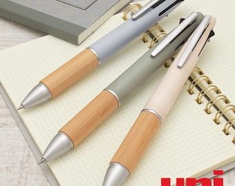 May include: Three multi-colored mechanical pencils with a bamboo-like design. The pencils are on a white notebook with gold spiral binding. The text "uni MITSUBISHI PENCIL" is printed on the notebook.