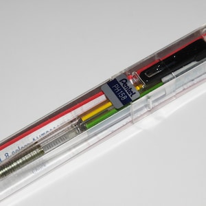 May include: A clear plastic case containing a silver mechanical pencil with a black and green colored lead holder. The case also contains a set of colored leads in red, yellow, green, and blue. The case has a label that reads " Pentel PH1158 ".