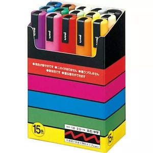 Peut inclure: Une bo&icirc;te de 15 marqueurs color&eacute;s avec une &eacute;tiquette noire et blanche indiquant "uni" sur chaque marqueur. La bo&icirc;te est orn&eacute;e de rayures jaunes, vertes, bleues, roses et rouges. La bo&icirc;te comporte &eacute;galement du texte japonais qui dit "15 couleurs" et "uni".