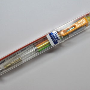 May include: A clear plastic package containing a Pentel PH158 8 colors automatic pencil. The pencil has a yellow and orange body with a clear plastic barrel. The package has red and white text that reads "Pentel 8 colors AUTOMATIC PENCIL PH158".