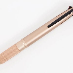 May include: A rose gold multi-function pen with a black retractable tip and a black clip. The pen has a textured grip.