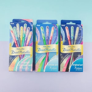 Pode incluir: Três caixas retangulares de cartão contendo canetas de gel Pentel Arts Dual Metallic. A caixa da esquerda contém 14 cores, enquanto as caixas central e direita contêm 7 cores cada. Embalagens com designs gráficos coloridos e texto.