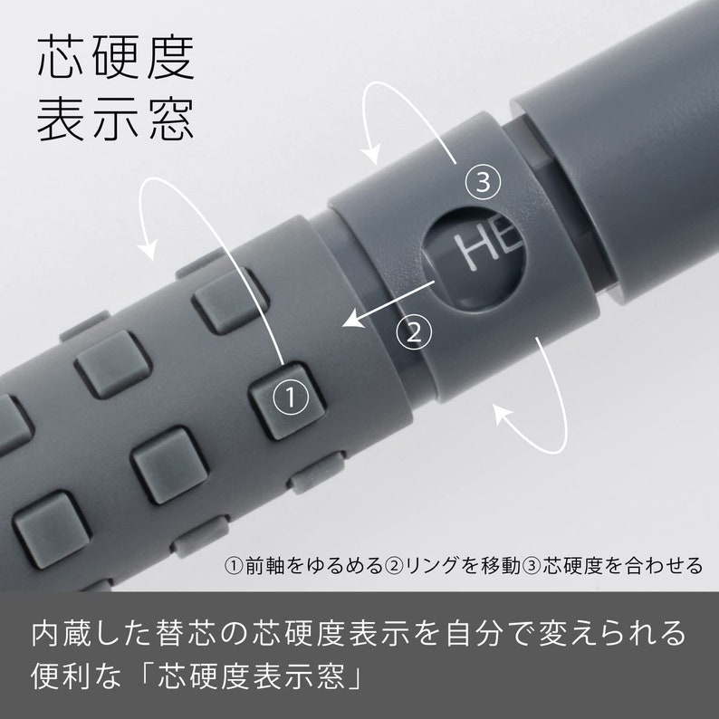 May include: Close-up of a gray mechanical pencil with a textured grip and a hardness indicator window. The pencil has a dial with the letters "HE" visible. Japanese text is also present.