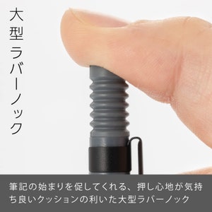 May include: A close-up of a gray rubber pen tip with a black clip. The pen tip has a ribbed design and is being pressed by a finger. Japanese text on the left says "Large rubber knock". Below, Japanese text describes the pen tip's comfortable cushion.