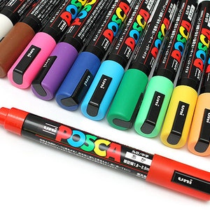 Peut inclure: Un ensemble de 15 marqueurs de peinture Posca de diff&eacute;rentes couleurs, dont le rouge, l'orange, le jaune, le vert, le bleu, le violet, le rose, le marron, le blanc et le gris. Les marqueurs sont dispos&eacute;s en rang&eacute;e, le rouge en t&ecirc;te. Les marqueurs sont tous &eacute;tiquet&eacute;s "Posca" et "uni".