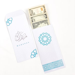 May include: White envelope with a blue and white geometric pattern and the word "MUBARAK" in Arabic script. The envelope is open and has cash inside.
