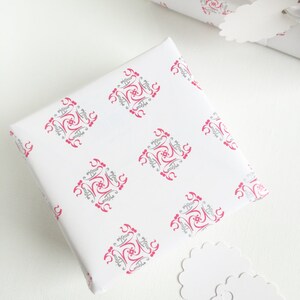 May include: Two white gift boxes with pink and gray patterned wrapping paper. The boxes are on a white surface with two white gift tags.