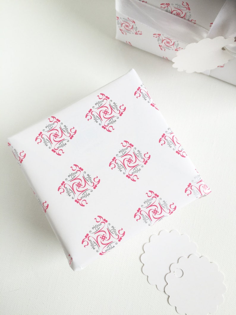 May include: Two white gift boxes with pink and gray patterned wrapping paper. The boxes are on a white surface with two white gift tags.