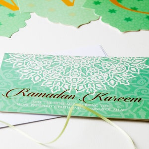 May include: A green card with a white mandala design and the text "Ramadan Kareem" in brown lettering. The text below reads "May the Holy Month bring you more prosperity, faith and blessings of Allah."