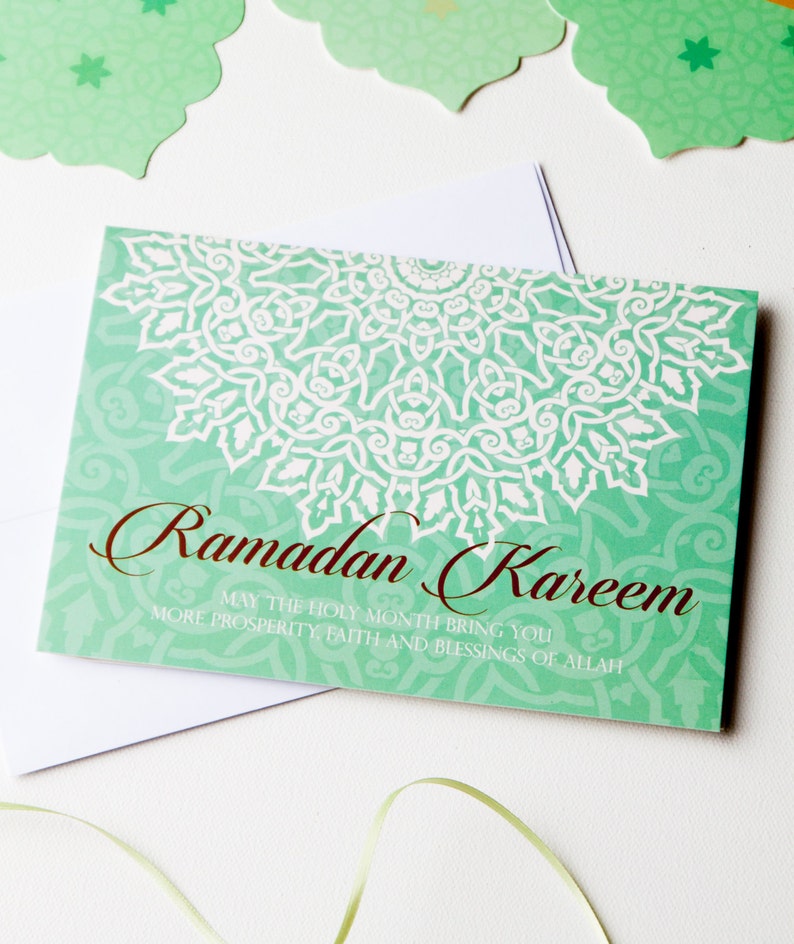 May include: A green card with a white mandala design and the text "Ramadan Kareem" in brown lettering. The card also includes the text "May the holy month bring you more prosperity, faith and blessings of Allah."