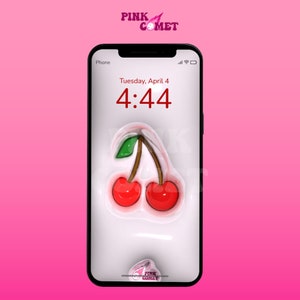 Puede incluir: Un tel&eacute;fono inteligente blanco con un marco negro muestra un emoji de cereza sobre un fondo blanco. La hora es 4:44 y la fecha es martes 4 de abril. El tel&eacute;fono est&aacute; sobre un fondo rosa.