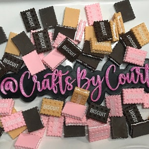 May include: A collection of miniature biscuit-shaped craft supplies in various colors. The biscuits are brown, tan, and pink, with the word "BISCUIT" printed on them. Some have a white filling. The image also includes the text "Crafts By Court".