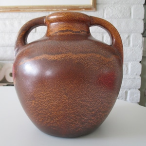 May include: A brown ceramic vase with two handles. The vase has a textured surface and a speckled brown glaze.